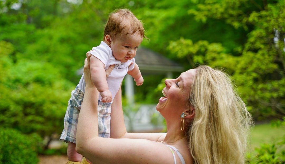 Consejos sobre pañales. Una madre sonriente alza a su bebé en el campo